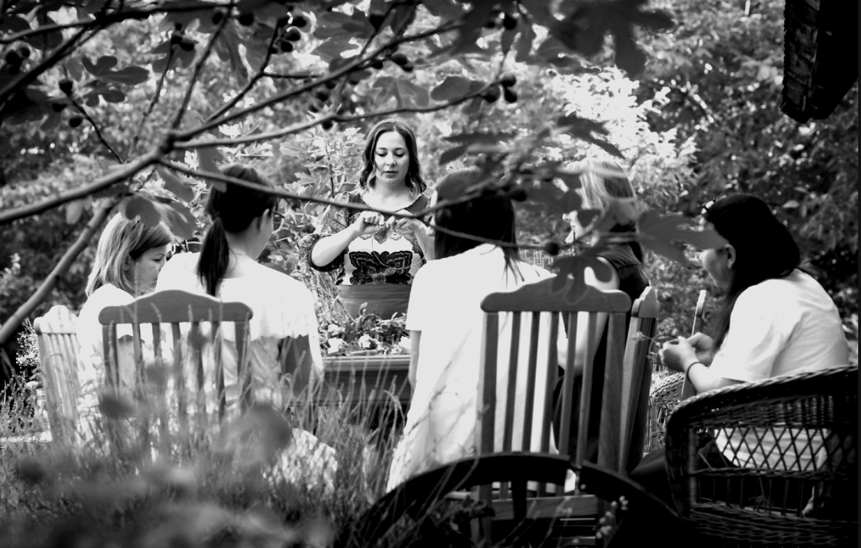 A small circle of women gathered at a garden table for a La Souveraine retreat, surrounded by greenery and poppies.